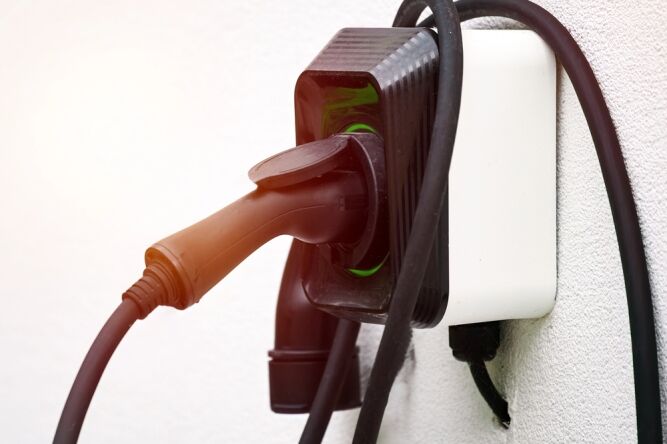 Close-up of an electric vehicle charging plug connected to a wall-mounted socket with cables draped over the device.