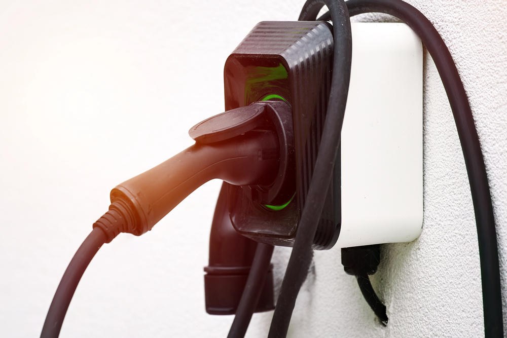 Close-up of an electric vehicle charging plug connected to a wall-mounted socket with cables draped over the device.