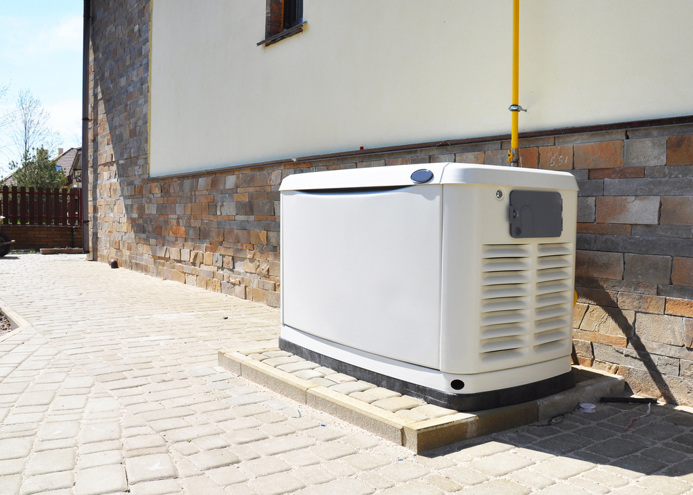 A standby generator is installed on a concrete pad next to a brick and stone exterior wall of a building.