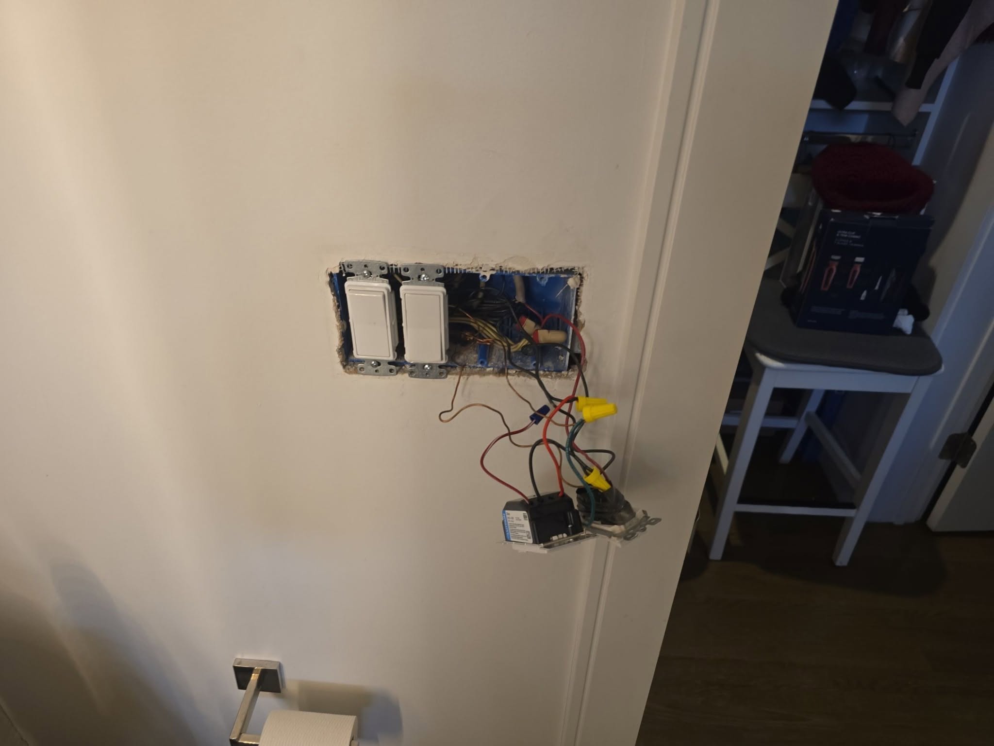 Wall light switch panel with two installed switches and one switch removed, exposing wires and wire nuts; electrical work in progress in a bathroom.